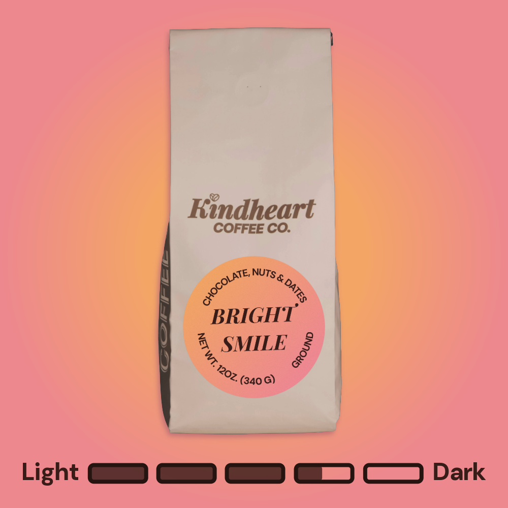 Kindheart Coffee Co. Bright Smile Blend Ground coffee bag on an pink and orange background with Medium Dark Roast bubbles 3.5 out of 5 roast level.