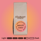Kindheart Coffee Co. Bright Smile Blend Whole Bean coffee bag on an pink and orange background with Medium Dark Roast bubbles 3.5 out of 5 roast level.