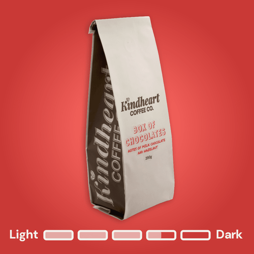 Kindheart Coffee Co. Box of Chocolates Blend coffee bag on a red background with Medium Dark Roast bubbles 3.5 out of 5 roast level.