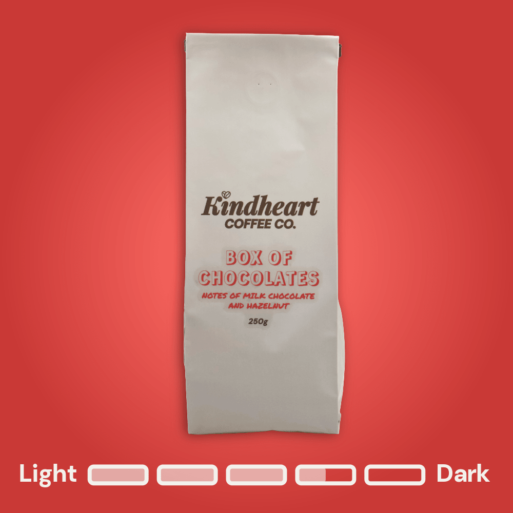 Kindheart Coffee Co. Box of Chocolates Blend coffee bag on a red background with Medium Dark Roast bubbles 3.5 out of 5 roast level.