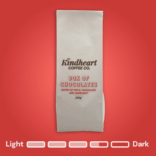 Kindheart Coffee Co. Box of Chocolates Blend coffee bag on a red background with Medium Dark Roast bubbles 3.5 out of 5 roast level.